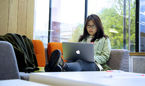 Student with laptop balanced on lap in study area