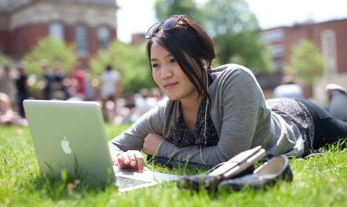 Student using laptop while lay on grass.